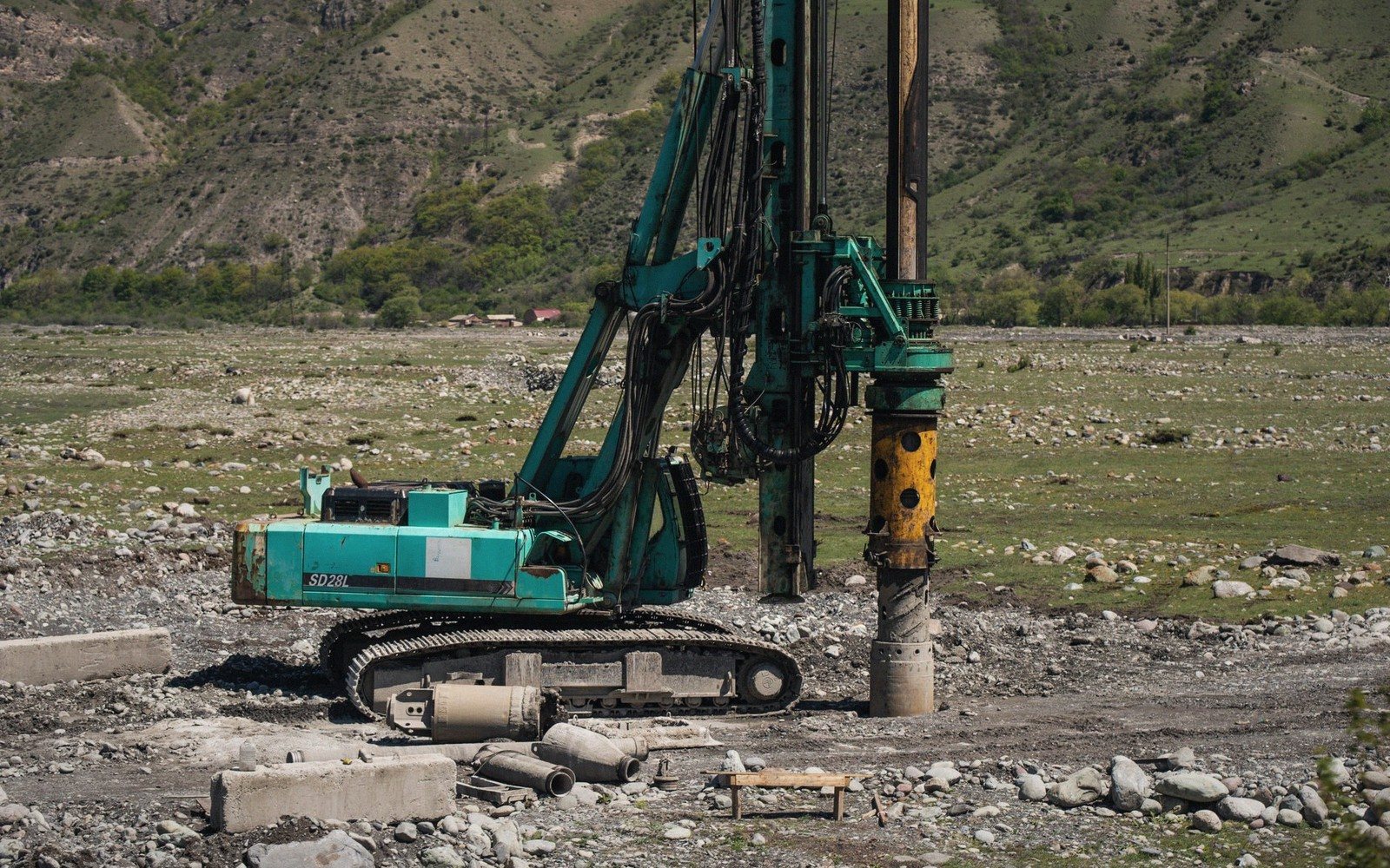 A crawler drilling rig bores a foundation pile on a rocky valley construction site
